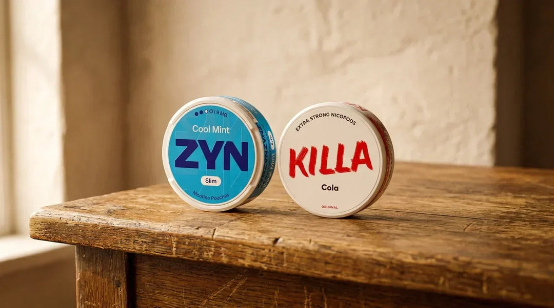 A can of Zyn and a can of Killa snus pouches standing side by side on a worn oak counter in soft window light
